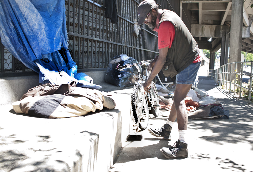 Beyond the structure: it is about forming shelter and having a place to call home. Shadow and his wife are homeless. She is not feeling well and is sleeping when we walk up. Shadow was cleaning up their area. He keeps a broom with them at all times to keep where they stay clean and they keep their belongings neatly statcked. They stay ready to move on a moments notice because they never know when the police will tell them the need to move. 