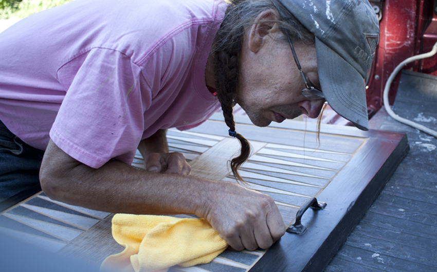 Mark Funk wipes down his handcrafted tile backgammon table as he prepares it for the caulk. He uses the caulk because he has grout in between tile and wood. which expand at different rates. The caulk will prevent it from cracking.Design by Mark Funk. Photo by Mary Anne Funk