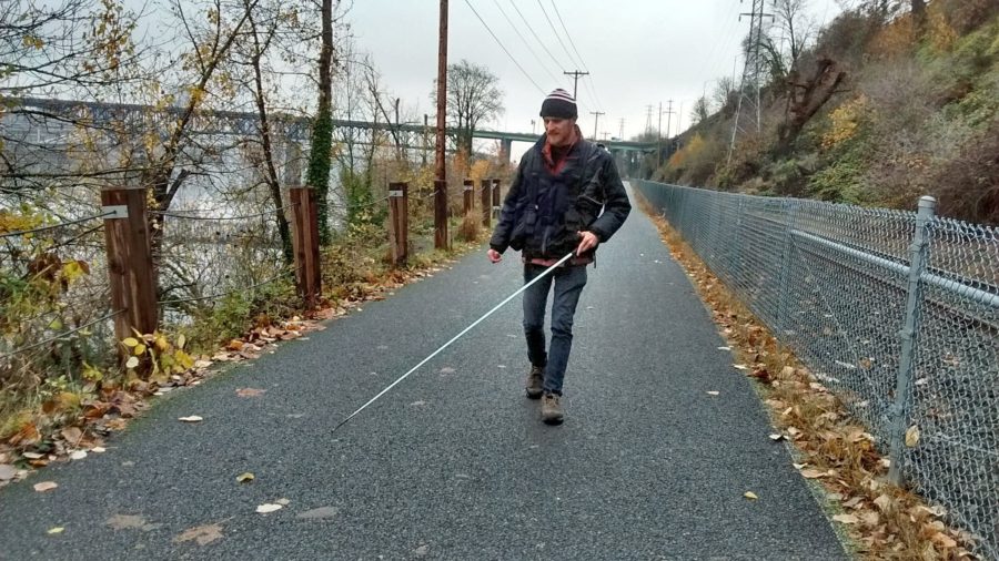 A blind man walks along a trail with his white cane